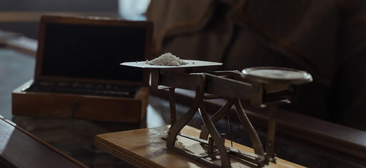 Classic vintage weighing scale with a small heap of white powder placed indoors on a wooden surface.