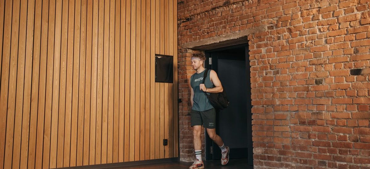A sporty man leaving a brick-walled sports hall, embodying active lifestyle and fitness.